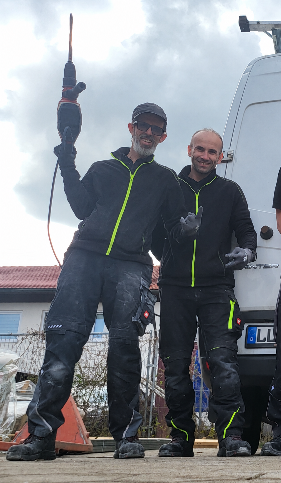 Zwei Kollegen in Arbeitskleidung im gemeinsamen Einsatz; einer hält einen Bohrhammer